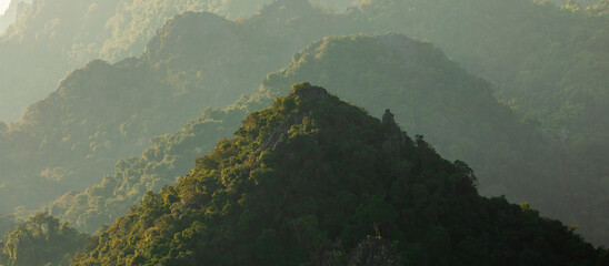 Pyramid-shaped hill, covered with lush rainforest at sunset, surrounded by higher mountains, near...