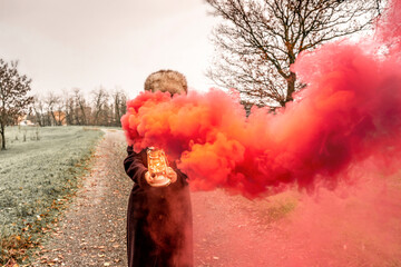 beautiful middle-aged woman on a country road showing a lantern that releases red smoke