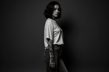 Obraz premium The woman stands confidently in a relaxed pose, showcasing her detailed tattoos while dressed in a simple t-shirt and jeans, illuminated against a dark background - Generative AI
