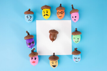 Fototapeta premium Colorful acorns with emoji faces on blue background. Autumn DIY craft idea, flat lay. Perfect for greeting cards, posters, banners, festive designs, and creative projects