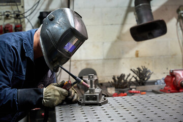 Metalworker welding custom mechanical part in workshop