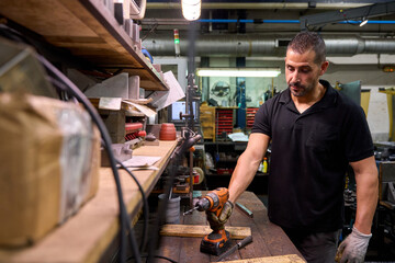 Metalworker using cordless drill in workshop creating custom mechanical parts