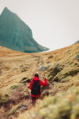 Fototapeta premium Girl traveler in a red jacket and with sticks goes down to the Kvalvika beach. Norway, Lofoten islands
