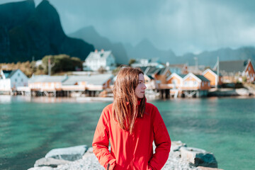 Traveler girl stands and enjoy the  beautiful colorful village Sakrisoy, Moskenes, Lofoten islands. Norway. Travel adventure Lifestyle concept