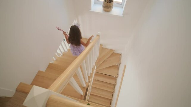 A little girl is walking down beautiful wooden stairs in a house.