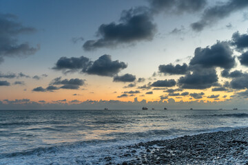 Obraz premium Sea waves roll onto the pebbly shore against the background of the evening sunset sky with clouds.