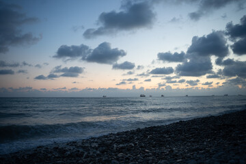 Sea waves roll onto the pebbly shore against the background of the evening sunset sky with clouds.