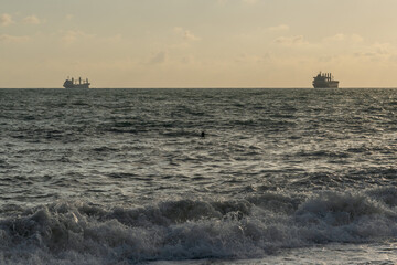 Sea waves roll onto the pebbly shore against the background of the evening sunset sky with clouds.