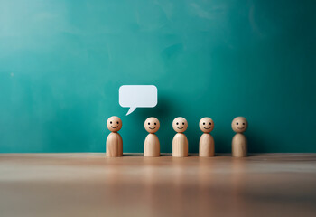 A row of wooden figures with happy faces stand before a blank speech bubble against a green background.