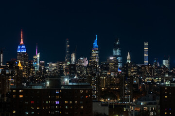 Fototapeta premium A stunning nighttime view of the New York City skyline with its iconic high-rise buildings illuminated in vibrant lights. The Empire State Building stands prominently with its colorful lights against 