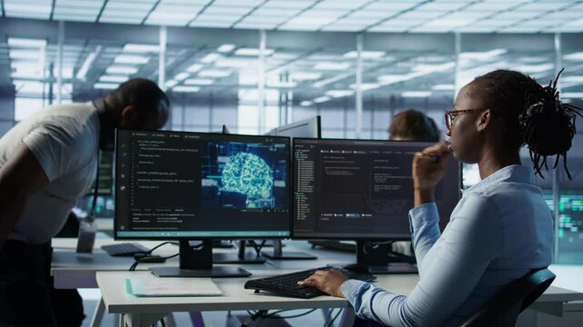 Engineer waiting at PC desk for checkup to be done on AI server room providing computing resources. African american woman investigating data center mainframes using computer, camera B