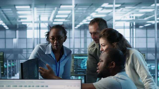 Multiethnic team of engineers working in server hub, using PCs to analyze data. Multiracial group of employees examining infrastructure in data center, ensuring system integrity and security, camera A
