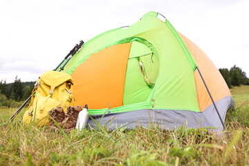 Tent, backpack, trekking poles and thermos on green grass in mountains