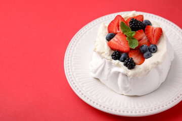 Pavlova cake (meringue dessert) with whipped cream, fresh berries and mint on red background, closeup. Space for text