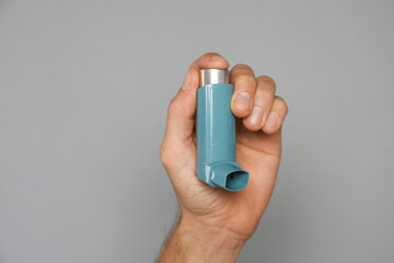 Man holding asthma inhaler on grey background, closeup