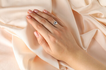 Woman wearing beautiful ring with gemstone against beige fabric, closeup