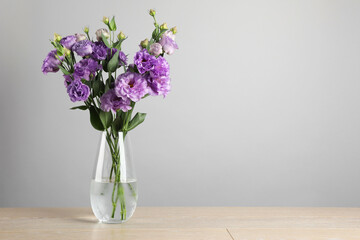 Vase with beautiful eustoma flowers on wooden table, space for text