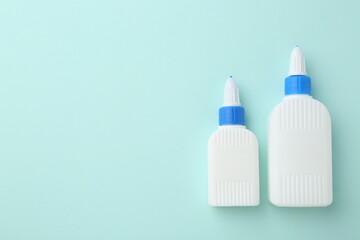 Bottles of glue on turquoise background, flat lay. Space for text