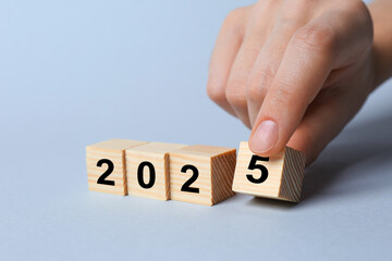 2025 New Year. Woman putting wooden cube with number 5 on light grey background, closeup