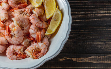 Boiled king prawns in deep bowl with lemon close up view on dark table
