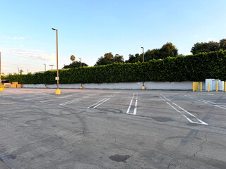urban parking lot - city car park - empty parking spaces, wall with hedges, bollards, street lights, trees in the background