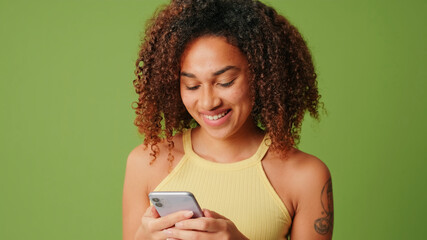 Young brunette isolated on green screen chroma key background with surprise expression while using smartphone, teenage girl surprised, happy and shocked. The person was told something good