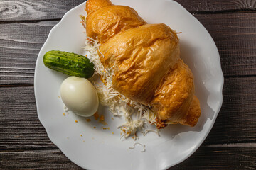 croissant sandwich with tuna, egg, cucumber on a white plate on a wooden table