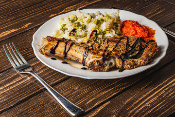 entrecote on the bone with rice and vegetables on a white plate, close-up view