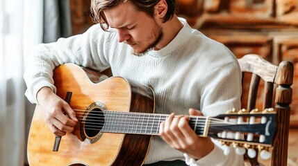 Obraz premium A focused man plays an acoustic guitar, sitting thoughtfully in a cozy, well-lit space, conveying passion for music.