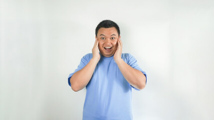 A young Indonesian man wearing a blue t-shirt with a surprised face facing forward