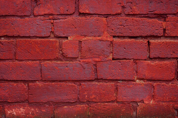 A fragment of a red brick wall with pronounced texture. Natural age defects in the form of cracks and abrasions. Rough surface with traces of dried paint.