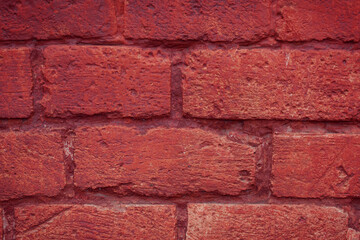 A fragment of a red brick wall with pronounced texture. Natural age defects in the form of cracks and abrasions. Rough surface with traces of dried paint.