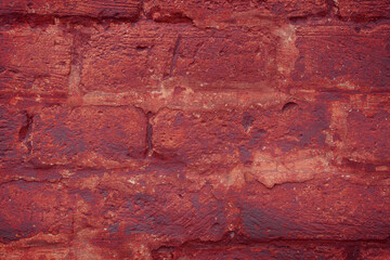 A fragment of a red brick wall with pronounced texture. Natural age defects in the form of cracks and abrasions. Rough surface with traces of dried paint.