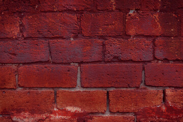 A fragment of a red brick wall with pronounced texture. Natural age defects in the form of cracks and abrasions. Rough surface with traces of dried paint.