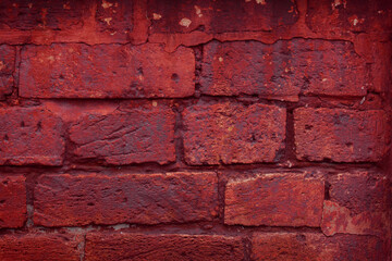 A fragment of a red brick wall with pronounced texture. Natural age defects in the form of cracks and abrasions. Rough surface with traces of dried paint.