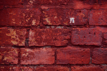 Obraz premium A fragment of a red brick wall with pronounced texture. Natural age defects in the form of cracks and abrasions. Rough surface with traces of dried paint.