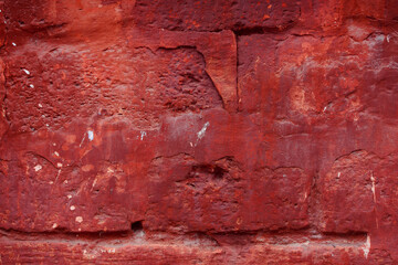 A fragment of a red brick wall with pronounced texture. Natural age defects in the form of cracks and abrasions. Rough surface with traces of dried paint.