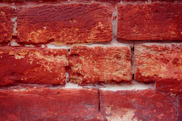 A fragment of a red brick wall with pronounced texture. Natural age defects in the form of cracks and abrasions. Rough surface with traces of dried paint.