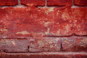 A fragment of a red brick wall with pronounced texture. Natural age defects in the form of cracks and abrasions. Rough surface with traces of dried paint.