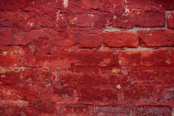 A fragment of a red brick wall with pronounced texture. Natural age defects in the form of cracks and abrasions. Rough surface with traces of dried paint.