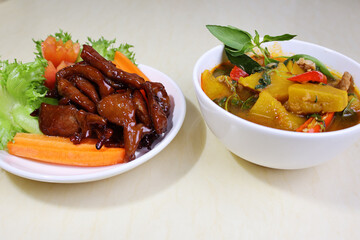 Pumpkin curry, pork, red chilli pieces on top Place the garnished basil shoots next to the white bowl. Place the fried pork on the side of the plate with the green vegetables, tomatoes, and carrots.

