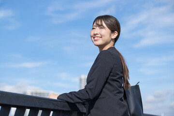 青空背景でスーツを着た笑顔の若い女性　就職や新卒採用のビジネスイメージ　未来や希望を見つめる