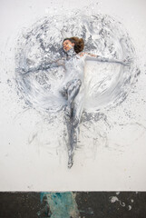 sexy nude woman lies covered in white and gray paint, creating a circular, abstract effect on the canvas around her. Her extended arms and serene expression evoke calm and unity with art.