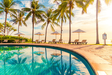 Beautiful luxury umbrella and chair around outdoor swimming pool in hotel and resort with coconut palm tree on sunset  or sunrise sky