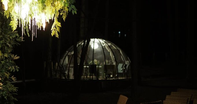 Night city. Beautiful lighting garlands hang from the trees illuminating the space next to the transparent igloo. Hand held. Siberia.
