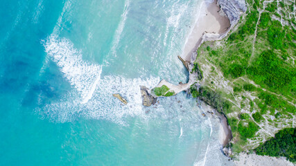 Aerial drone view of turquoise sea water meeting a rocky coastline on a sunny summer day © Balnyes Visuals