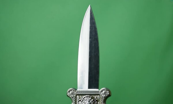 Sleek Silver Dagger Spinning with Reflective Blade and Intricate Hilt on Green Screen