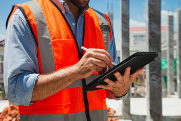 A man in an orange safety vest is using a tablet to take notes. Concept of caution and safety in a potentially hazardous environment