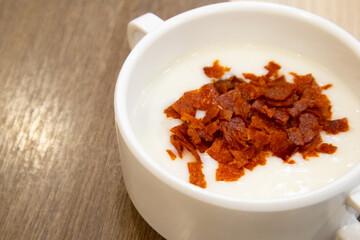 Mushroom cream soup topping with bacon bits in white soup bowl on wooden background