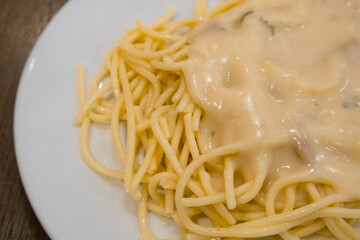 Spaghetti topping with cream of mushroom soup serving on white dish on wooden background. Traditional food in Italy.